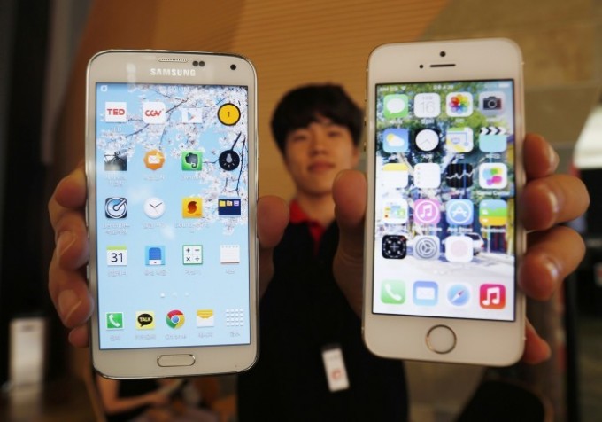 A sales assistant holding Samsung Electronics' Galaxy 5 smartphone (L) and Apple Inc's iPhone 5 smartphone (R) poses for photographs at a store in Seoul July 16, 2014.  REUTERS/KIM HONG-JI