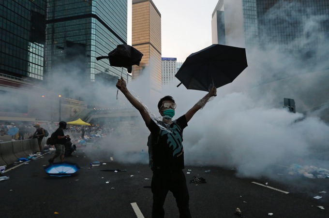 A protester (C) raises his umbrellas in front of tear gas which was fired by riot police to disperse protesters blocking the main street to the financial Central district outside the government headquarters in Hong Kong, September 28, 2014. Hong Kong police used tear gas for the first time on Sunday to disperse pro-democracy protests and baton-charged the crowd blocking a key road in the government district after Hong Kong and Chinese officials warned against demonstrations. [REUTERS/Tyrone Siu]