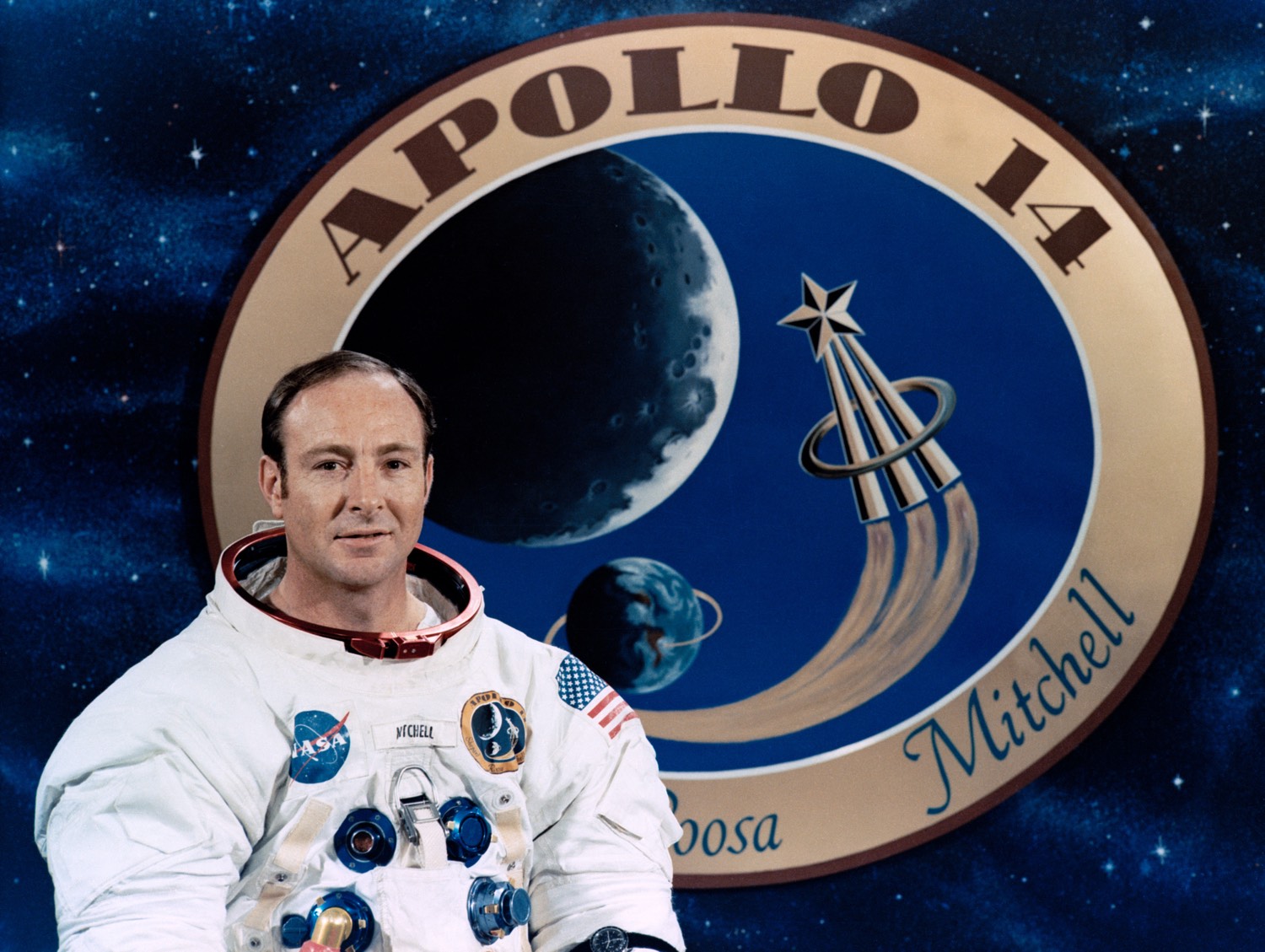 Apollo astronaut Edgar Mitchell in front of a graphic of the mission patch. [NASA]