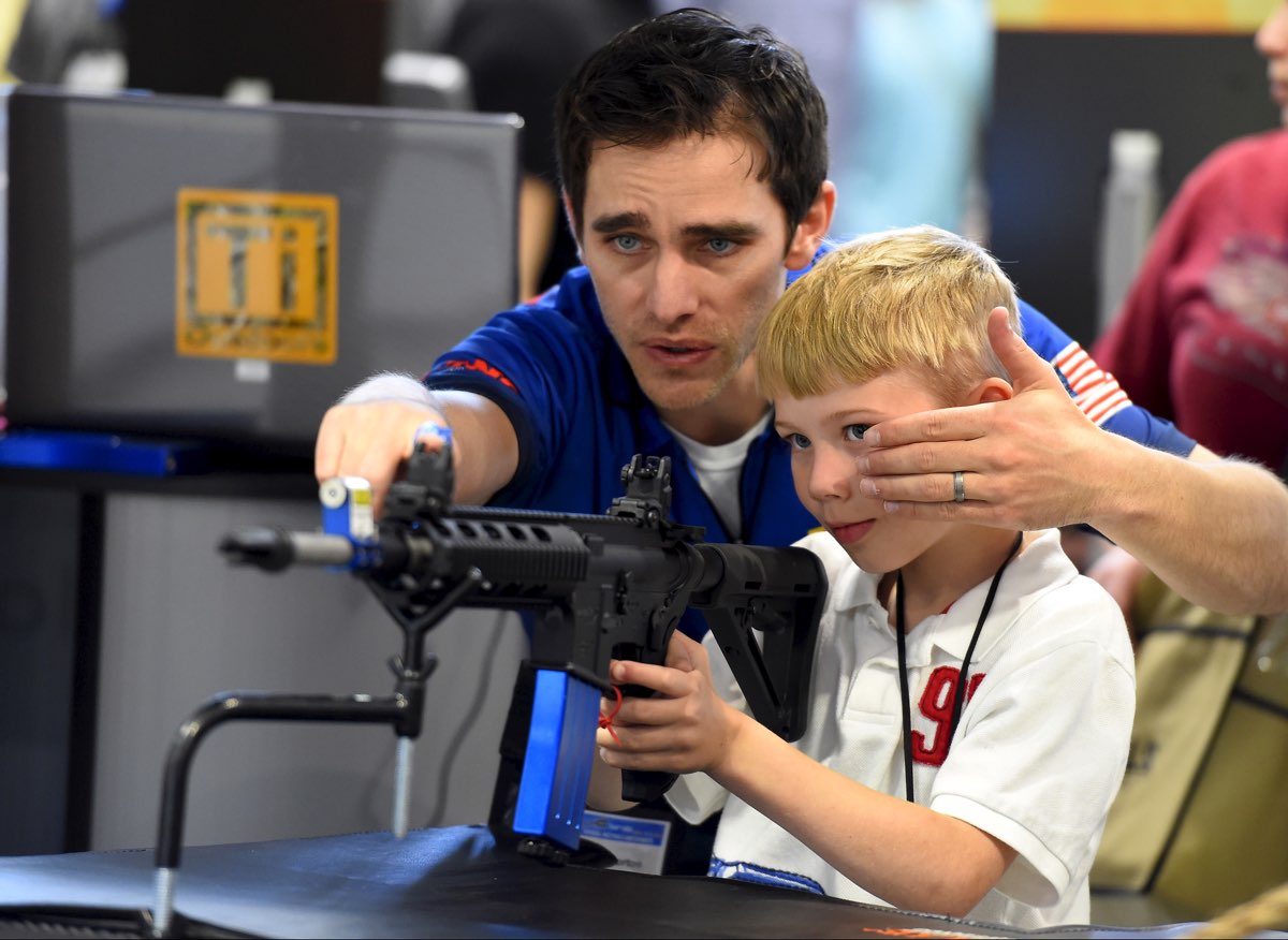 A man shows a boy how to sight down an electronic rifle at an NRA meeting. [Reuters]
