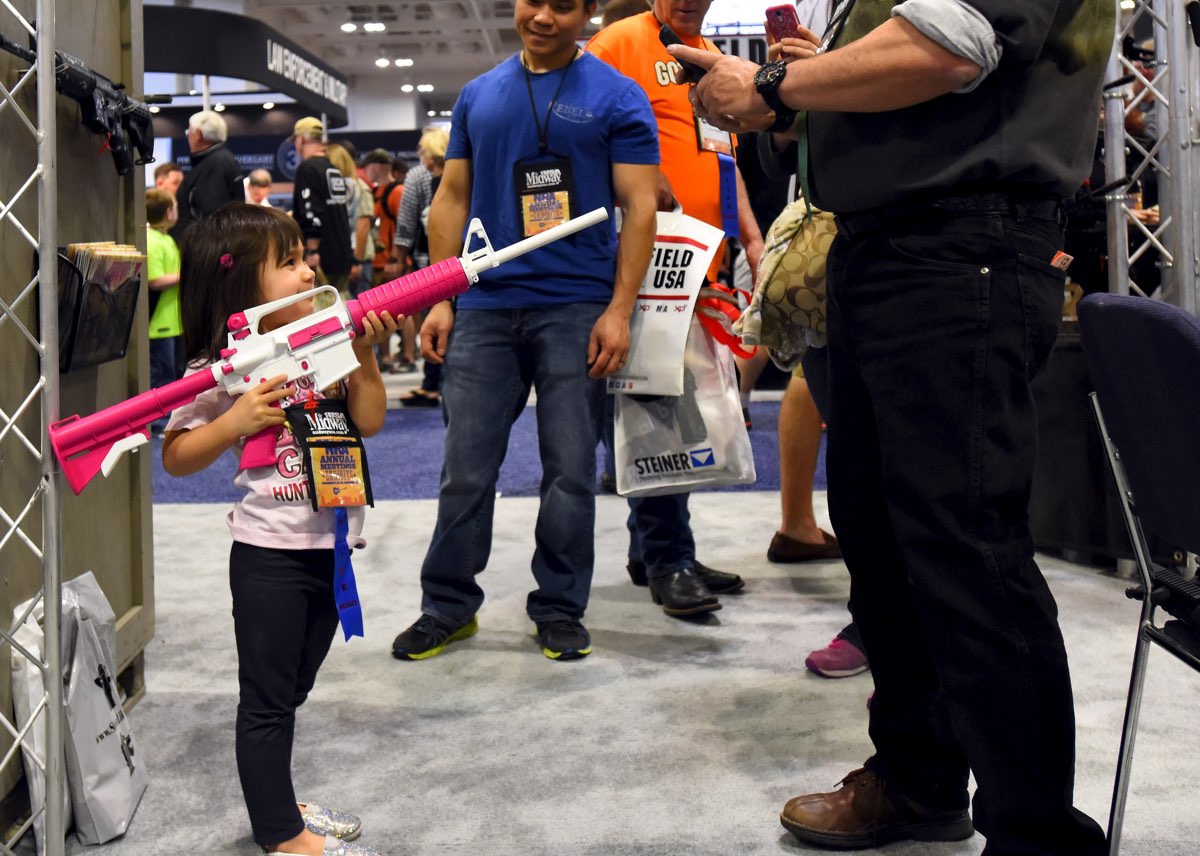 A young NRA member, gets her photo with a non-toy rifle  at an NRA convention [REUTERS]